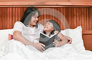 Happy mother and daughter reading book on bed