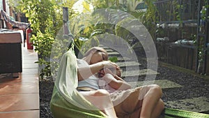 Happy mother and daughter relaxing together in a hammock at garden in summer day