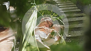 Happy mother and daughter relaxing together in a hammock at garden in summer day