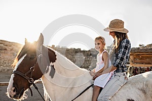 Happy mother and daughter riding a horse at sunset - Main focus on woman