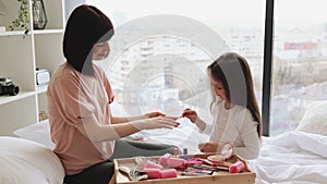 Happy mother and daughter sitting in bed at home and doing manicure.