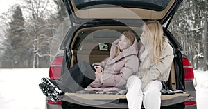 Happy mother and daughter sitting in car trunk