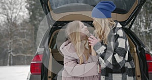 Happy mother and daughter sitting in car trunk