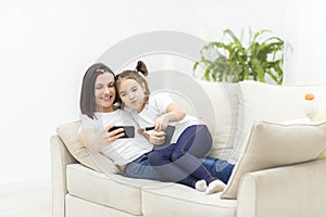 Happy mother and daughter sitting on the couch and taking selfie in the living room.