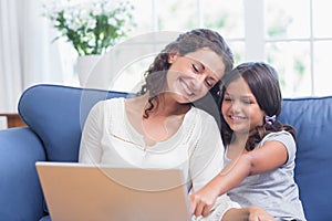 Happy mother and daughter sitting on the couch and using laptop