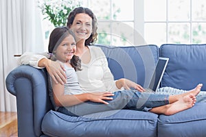 Happy mother and daughter sitting on the couch and using laptop