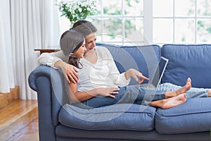 Happy mother and daughter sitting on the couch and using laptop