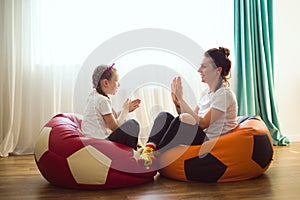 Happy mother and daughter are sitting on football bin bags and playing