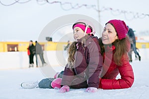 Happy mother and daughter sitting on the outdoor rink