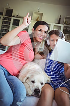 Happy mother and daughter sitting with pet dog and using digital