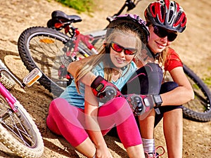 Happy mother and daughter are sitting on road near bicycles.