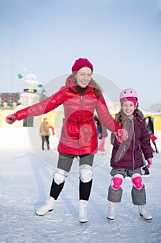 Happy mother and daughter are skating atoutdoor skating rink