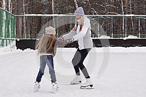 Happy mother and daughter skating on a outdoor skating rink