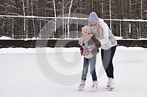 Happy mother and daughter skating on a outdoor skating rink