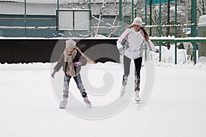 Happy mother and daughter skating on a outdoor skating rink