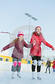 Happy mother and daughter are skating at outdoor skating rink