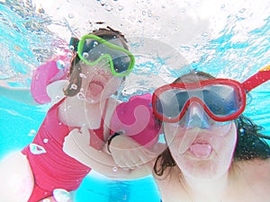 Happy mother and daughter sticking out their tonge, swim underwater in a swimming pool. Holidays and vacations, summer time. photo