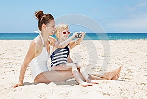 Happy mother and daughter in swimsuits taking photos at beach