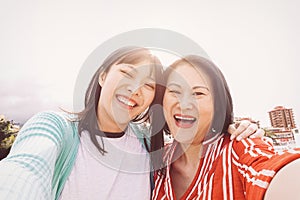 Happy mother and daughter taking selfie with mobile smartphone outdoor - Asian family sharing time and photo together