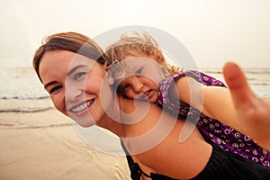 Happy mother and daughter taking selfie photo with smartphone on the Sunset beach. woman having fun with her kid on