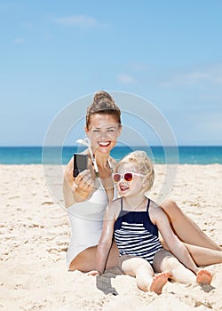 Happy mother and daughter taking selfies with camera at beach