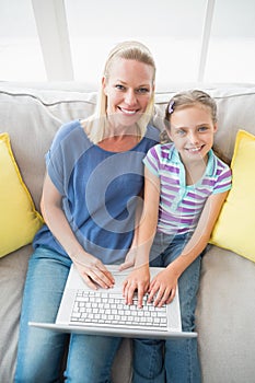 Happy mother and daughter using laptop on sofa