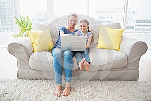 Happy mother and daughter using laptop on sofa