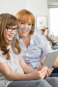 Happy mother and daughter using tablet PC with family sitting in background at home