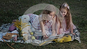 A happy mother and daughter view photos in an album read a book. Family in a city park on a picnic on a warm evening at