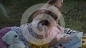 A happy mother and daughter view photos in an album read a book. Family in a city park on a picnic on a warm evening at