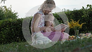 A happy mother and daughter view photos in an album read a book. Family in a city park on a picnic on a warm evening at