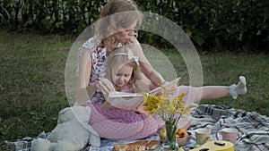 A happy mother and daughter view photos in an album read a book. Family in a city park on a picnic on a warm evening at