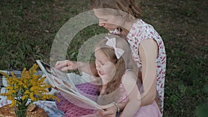 A happy mother and daughter view photos in an album read a book. Family in a city park on a picnic on a warm evening at