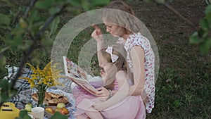 A happy mother and daughter view photos in an album read a book. Family in a city park on a picnic on a warm evening at