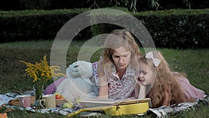 A happy mother and daughter view photos in an album read a book. Family in a city park on a picnic on a warm evening at