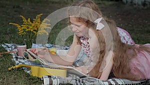 A happy mother and daughter view photos in an album read a book. Family in a city park on a picnic on a warm evening at