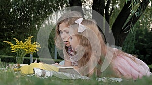 A happy mother and daughter view photos in an album read a book. Family in a city park on a picnic on a warm evening at