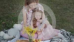 A happy mother and daughter view photos in an album read a book. Family in a city park on a picnic on a warm evening at