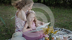 A happy mother and daughter view photos in an album read a book. Family in a city park on a picnic on a warm evening at