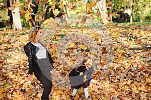 Happy mother and daughter walking in autumn park. Autumn time, weekend and holidays. Family throwing autumn leaves