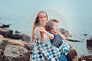 Happy mother and daughter wrapped in quilt blanket spending time together on the beach on summer vacation. Happy family traveling