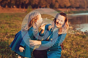 Happy mother and daugter having fun together at nature. Family on autumn walk. Little pretty girl blowing dandelion on her mom