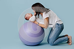 Happy mother doing exercises with her infant child baby on purple yoga ball