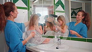 Happy mother is drying child daughter hair after shower standing in front of a mirror in the bathroom