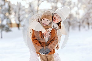 Happy mother embracing little boy son while having fun in snowy weather outdoor