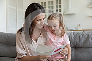 Happy mother embracing little daughter, reading greeting card