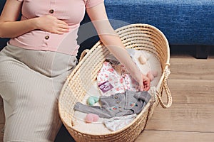 Happy mother enjoying pregnancy. Wicker basket of cute tiny stuff newborn. Beautiful pregnant woman at home