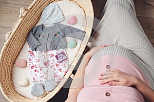 Happy mother enjoying pregnancy. Wicker basket of cute tiny stuff newborn. Beautiful pregnant woman at home