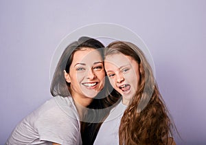 Happy mother and excited joying kid girl hugging with emotional smiling faces on purple background with empty copy space. Closeup