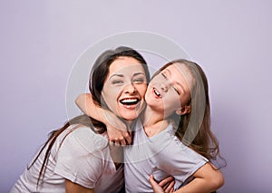 Happy mother and excited joying kid girl hugging with emotional smiling faces on purple background with empty copy space